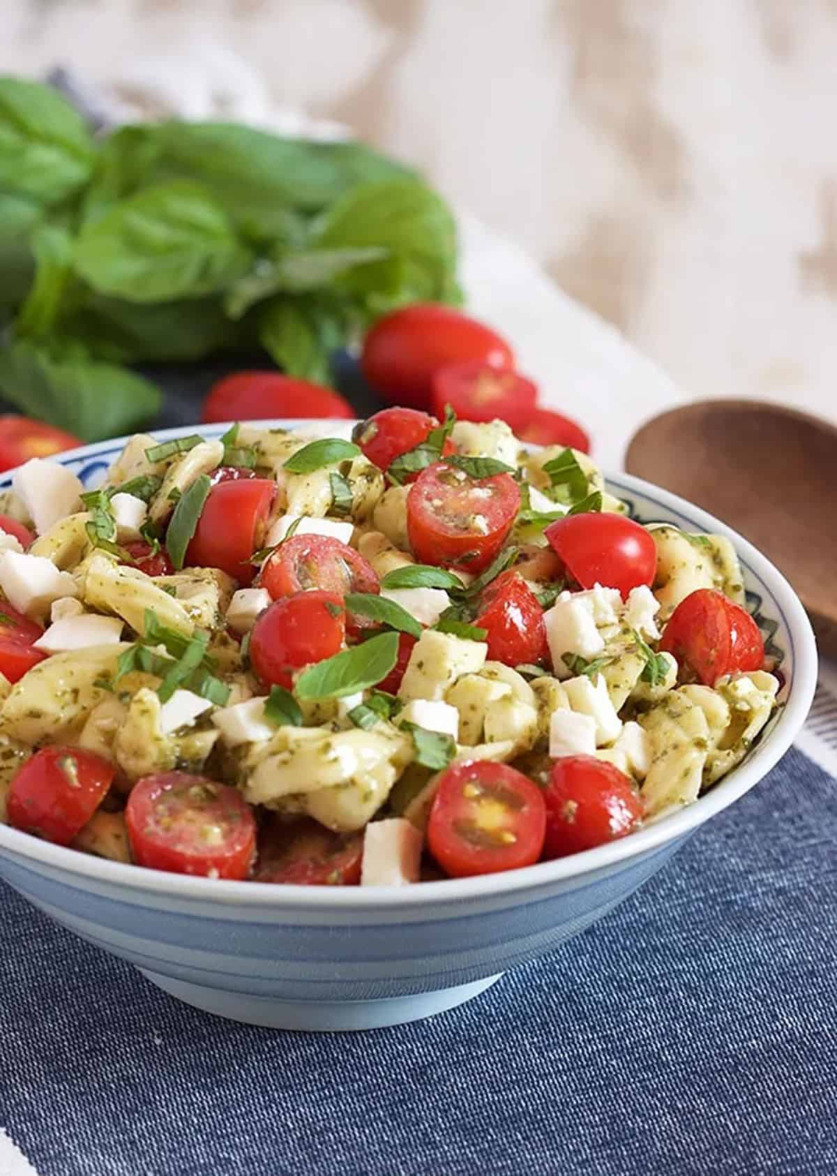 Bowl of Caprese Tortellini salad with basil and tomatoes in the background.