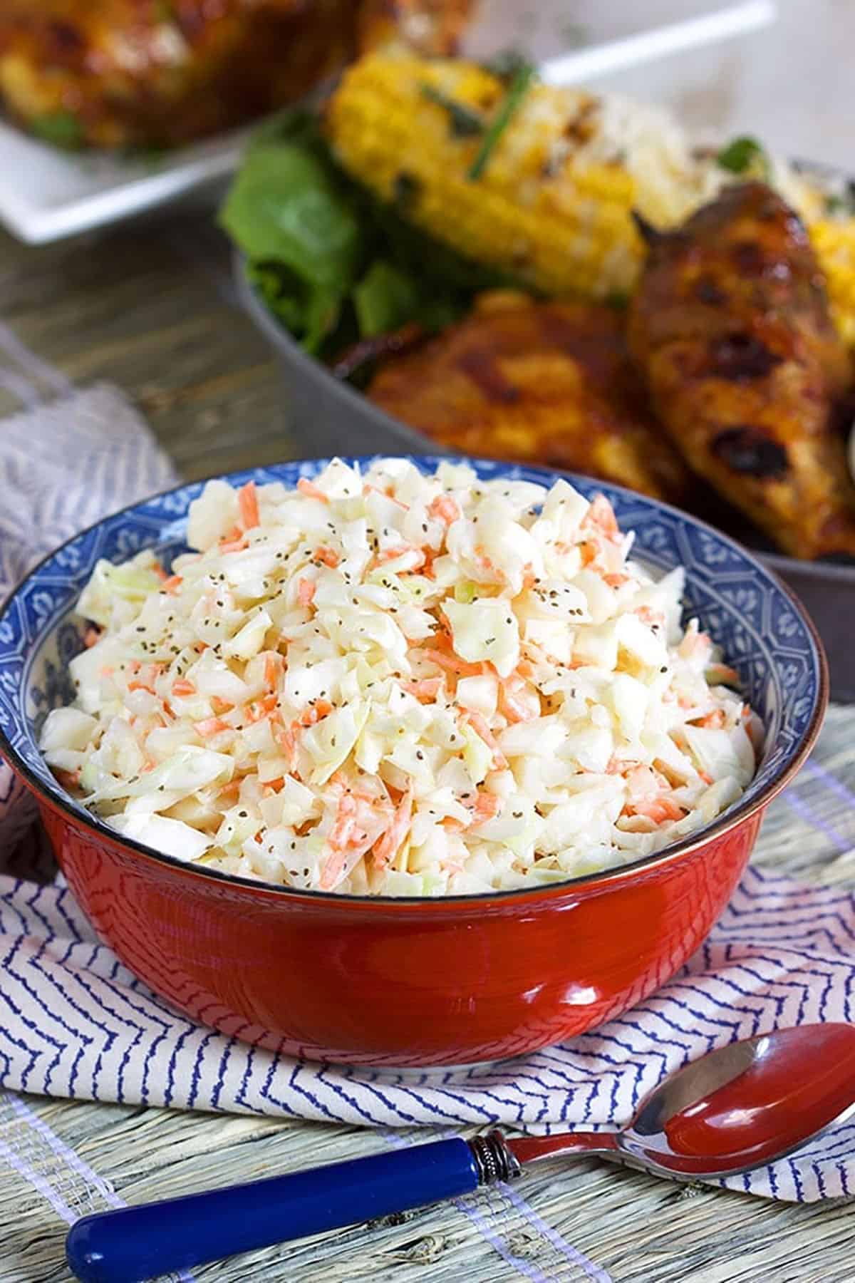 Coleslaw in a red bowl with bbq chicken in the background.