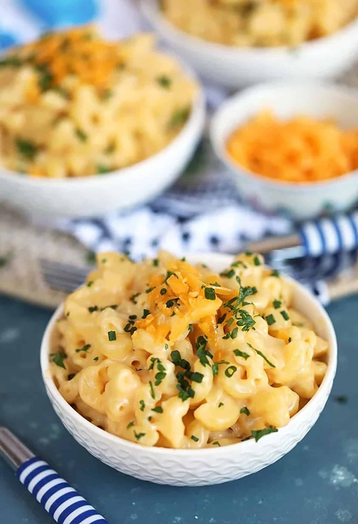 macaroni and cheese in a white bowl on a blue background with a small bowl of cheddar behind it.