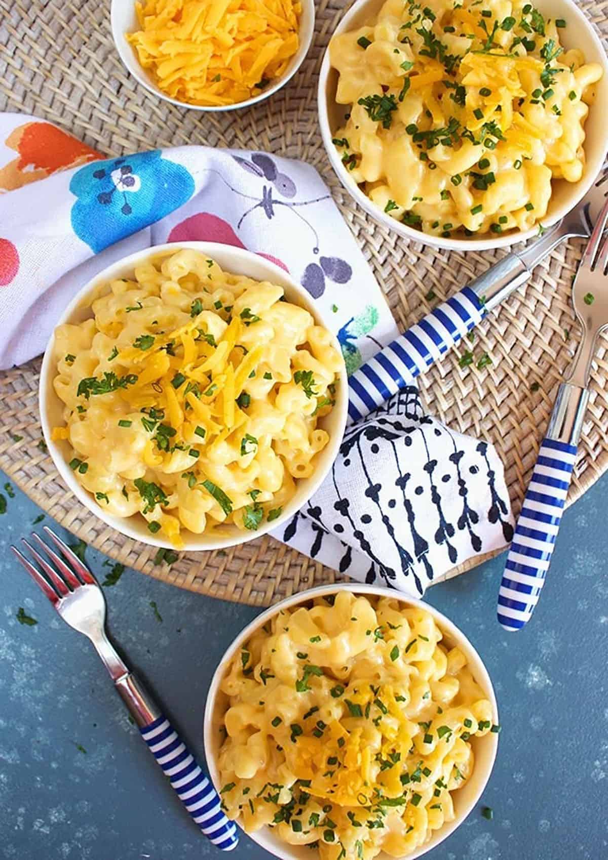 Overhead shot of three bowls of easy Mac and cheese recipe on a blue background with a floral napkin 