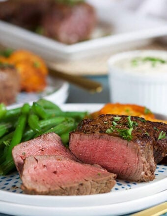 Filet mignon sliced on a white plate with green beans.