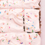 A frosted, sprinkled, and sliced sheet cake is presented on a white surface.