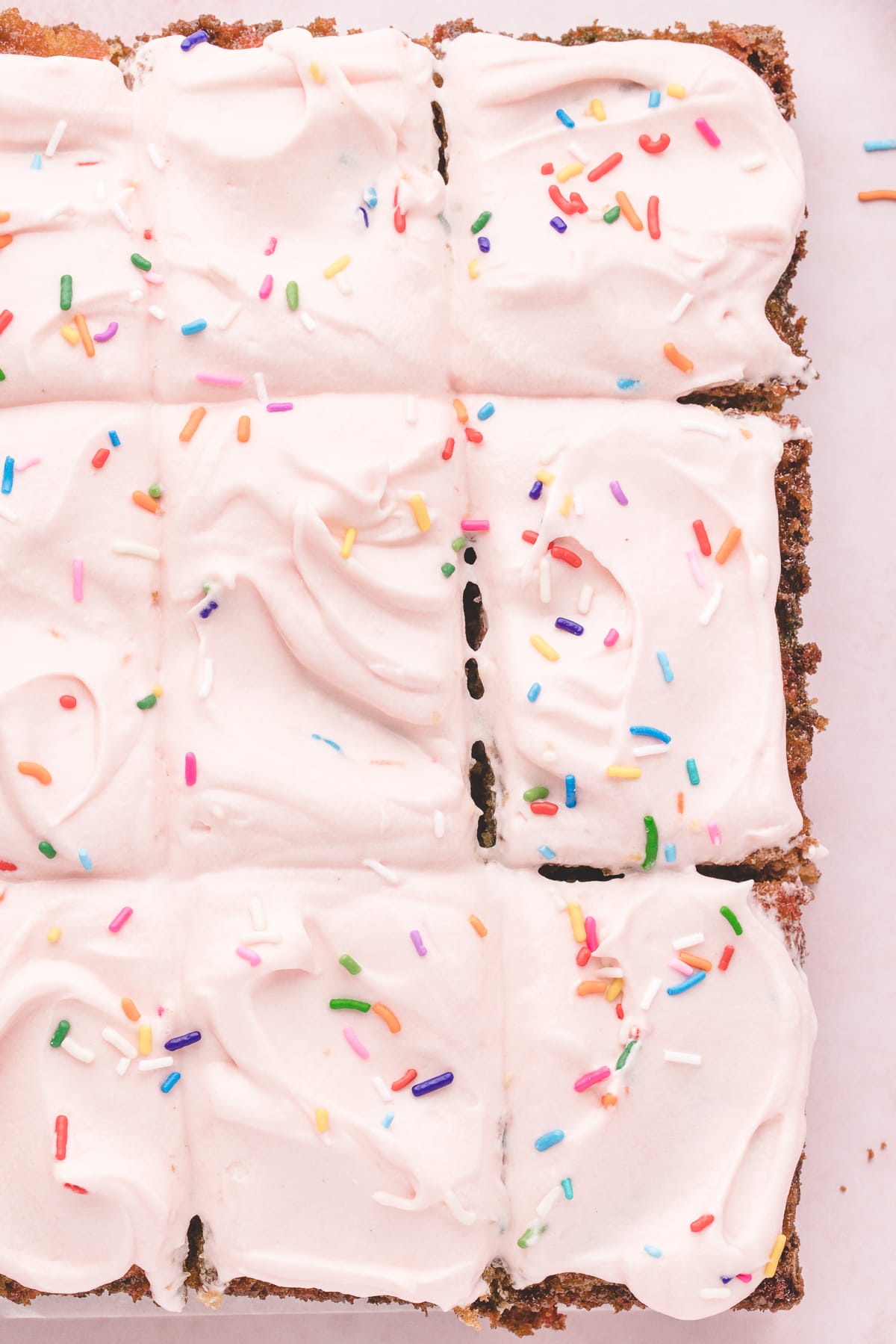 A frosted, sprinkled, and sliced sheet cake is presented on a white surface.