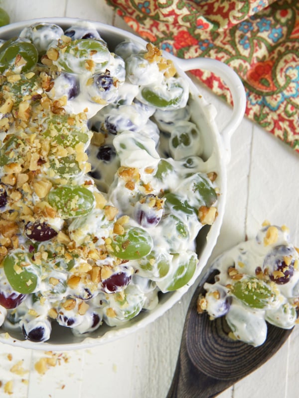 A wooden spoon has scooped out a serving of grape salad from the bowl.