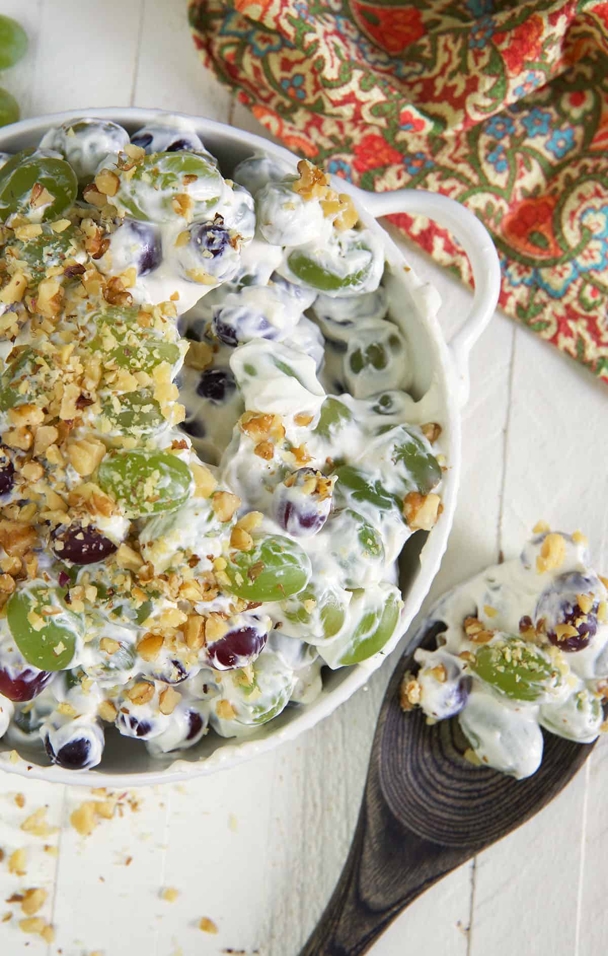 A wooden spoon has scooped out a serving of grape salad from the bowl.