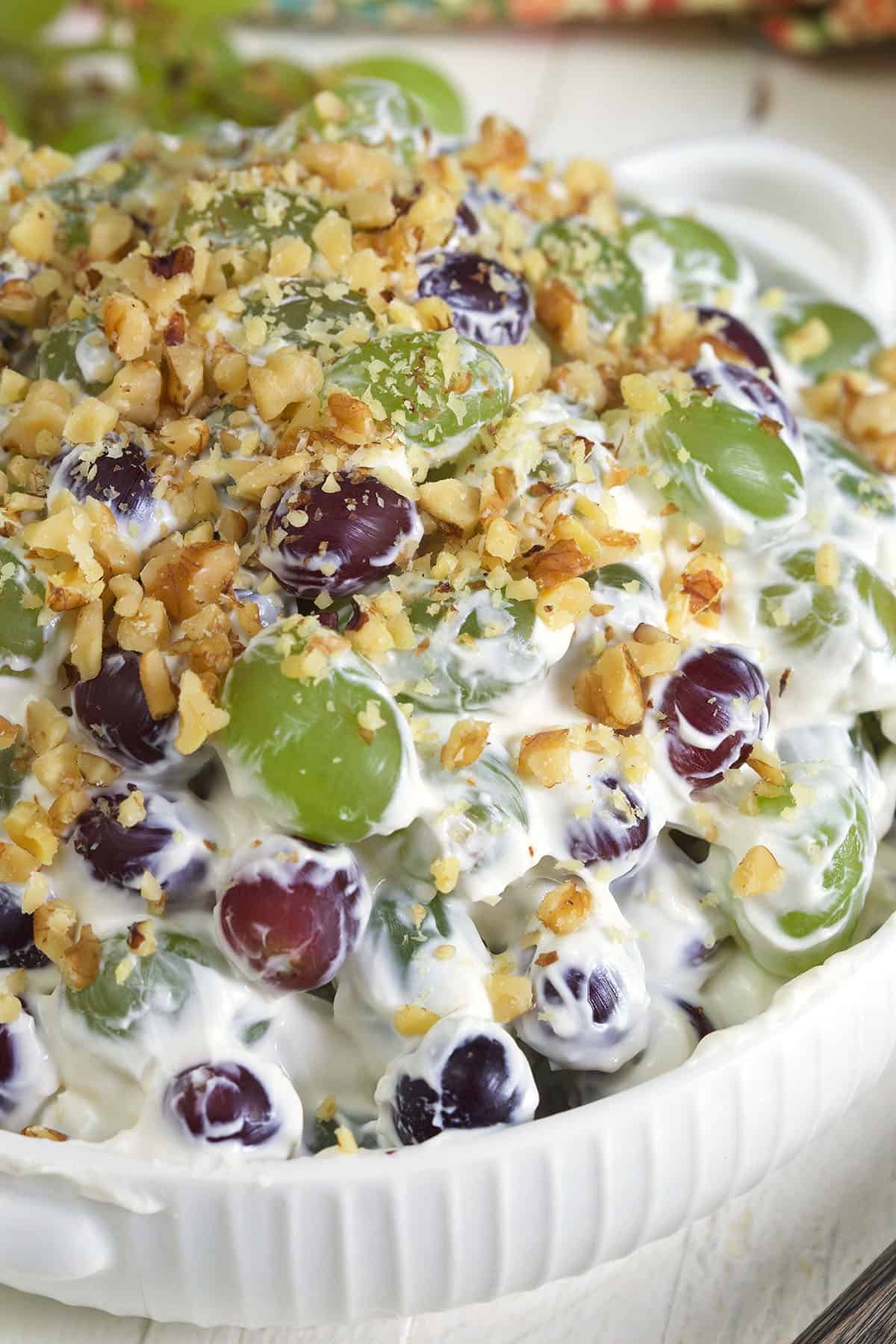A white bowl is filled with grape salad that's topped with crunchy walnuts.