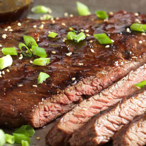Flank steak sliced on a pewter tray with sesame seeds and chopped green onion on top.