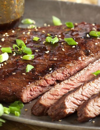 Flank steak sliced on a pewter tray with sesame seeds and chopped green onion on top.