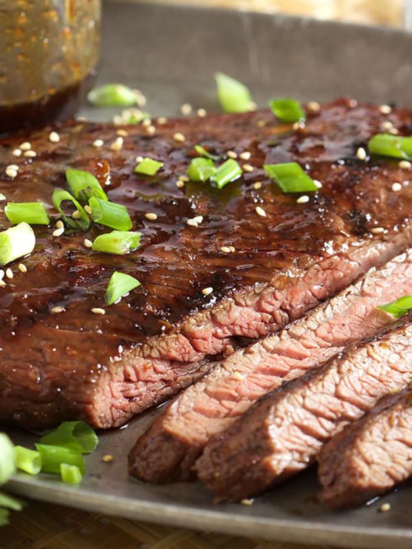 Flank steak sliced on a pewter tray with sesame seeds and chopped green onion on top.