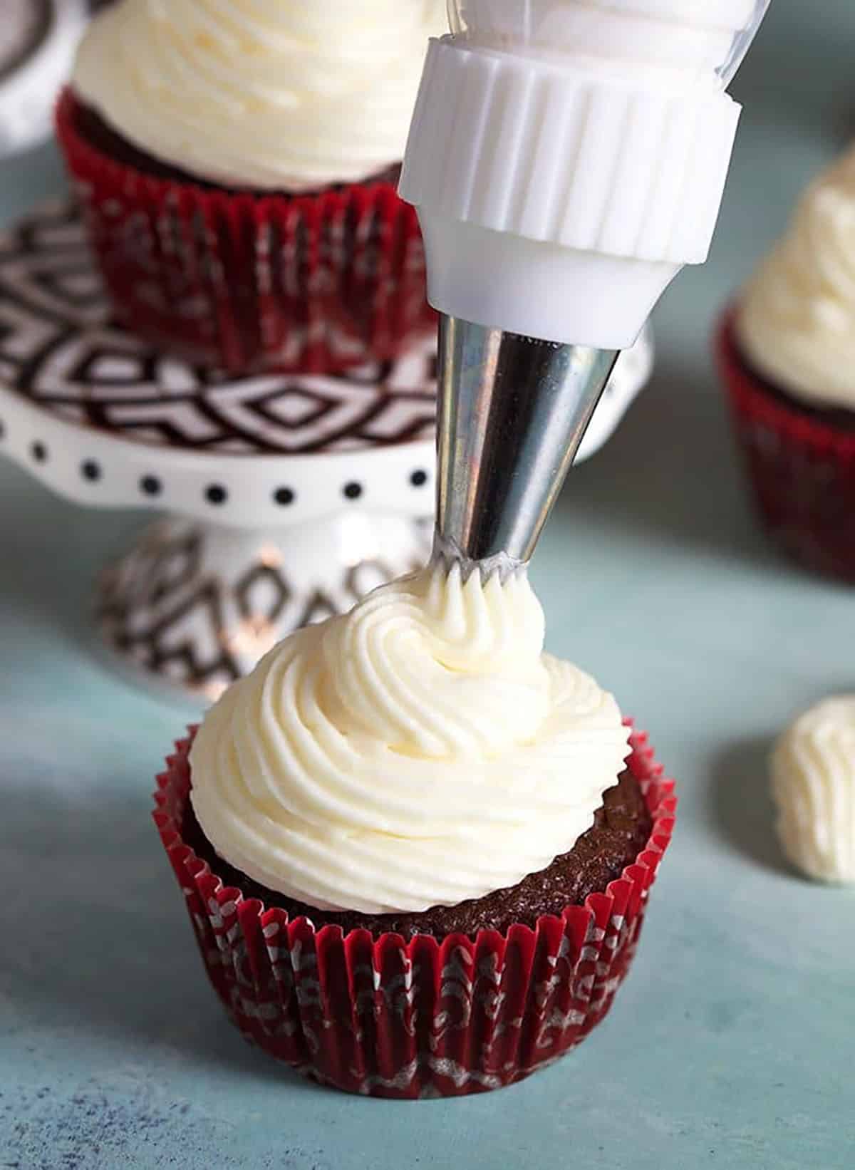 Cream cheese frosting being piped onto a chocolate cupcake.