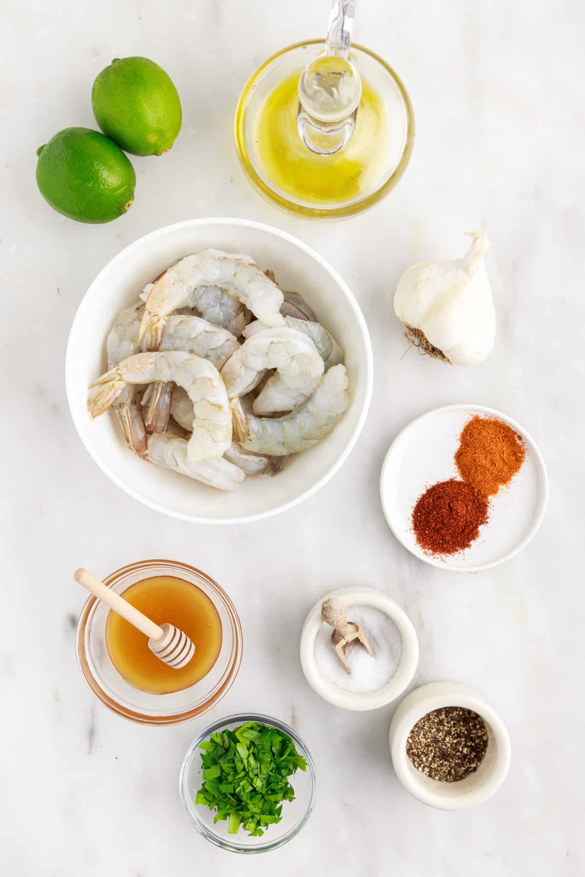 The ingredients for honey lime shrimp are spread out across a white surface.