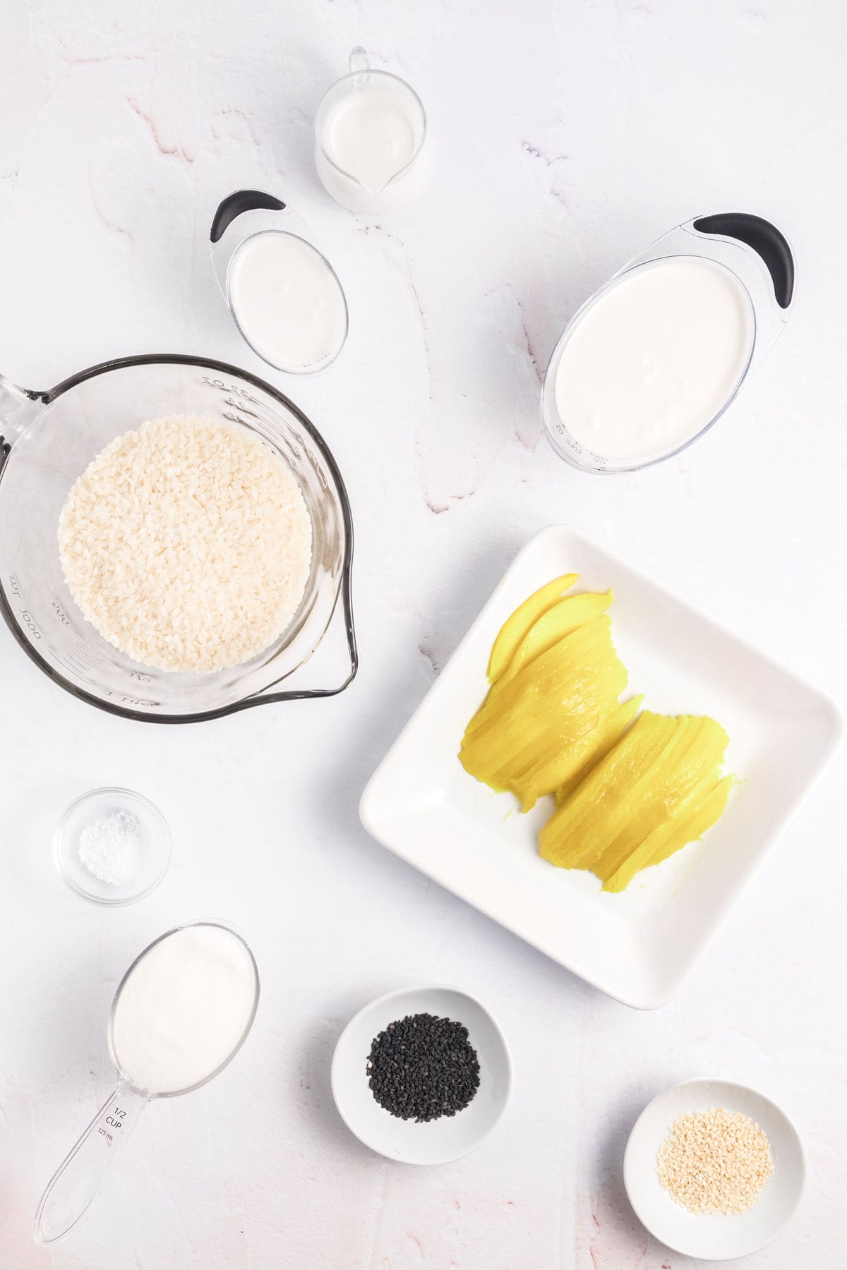 The ingredients for mango sticky rice are presented on a white countertop. 
