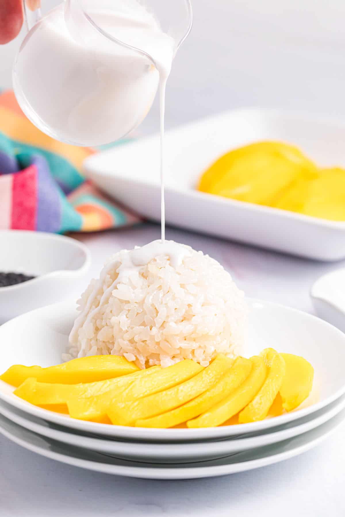 Coconut milk is being drizzled onto a serving of mango sticky rice.