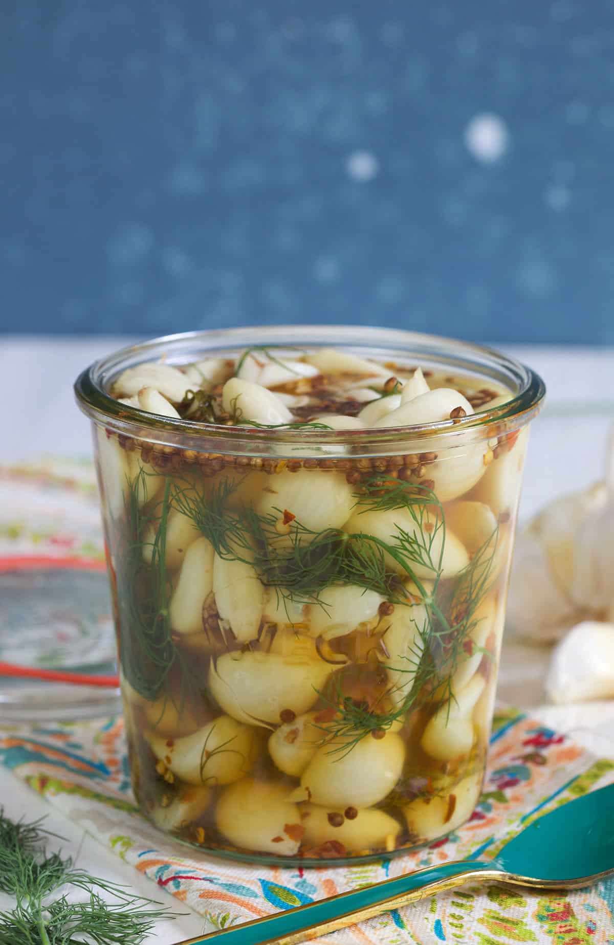 An open jar of pickled garlic is presented on a white and blue surface.