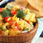 Pineapple Salsa in a wooden bowl with chips in the background.