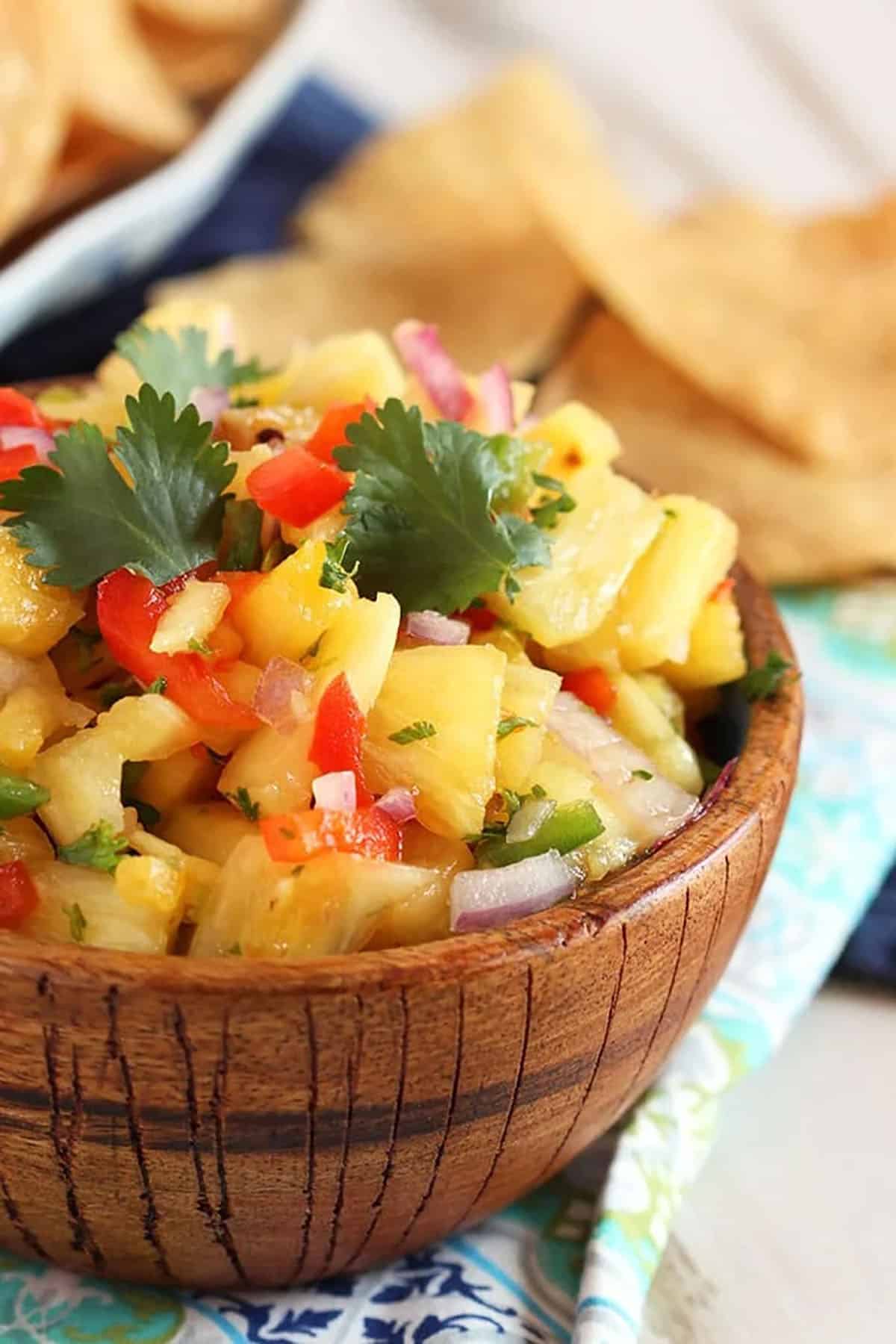Pineapple Salsa in a wooden bowl with chips in the background.