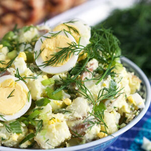 Potato salad in a blue and white bowl with dill and egg.
