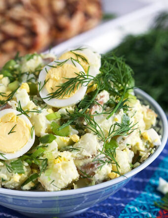 Potato salad in a blue and white bowl with dill and egg.