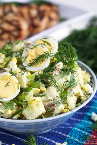 Potato salad in a blue and white bowl with dill and egg.