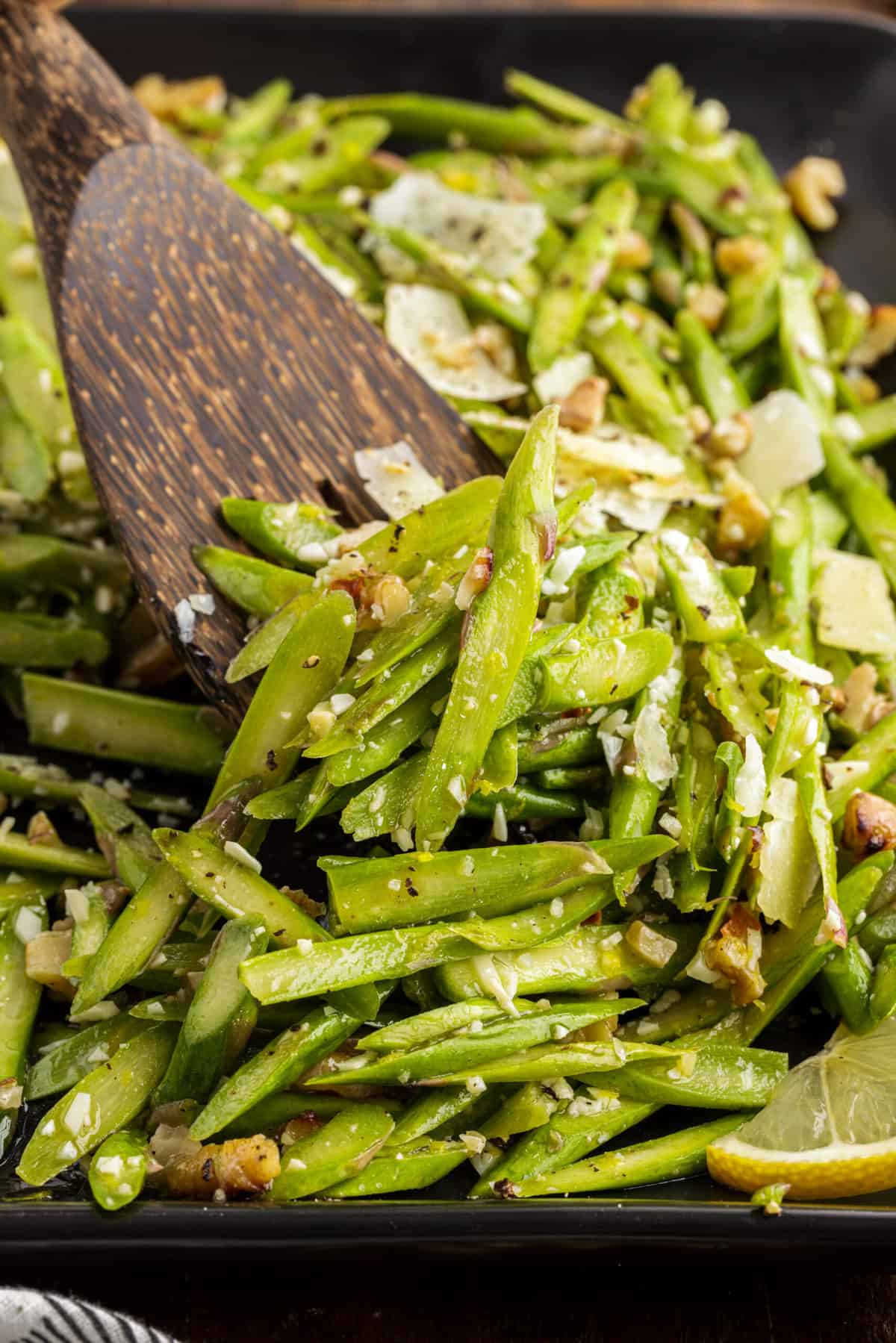 A wooden spoon is mixing asparagus with the dressing.