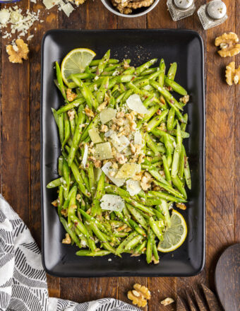 A rectangular black serving plate is filled with fresh raw asparagus salad.