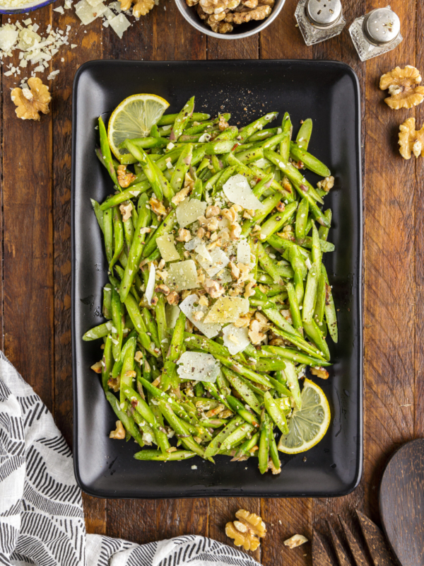 A rectangular black serving plate is filled with fresh raw asparagus salad.