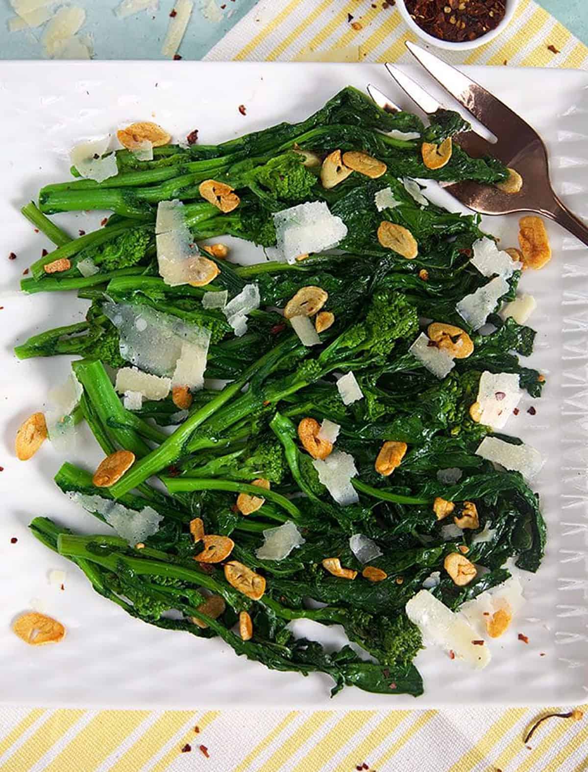 Broccoli rabe on a white square platter with crushed red pepper flakes in a bowl.