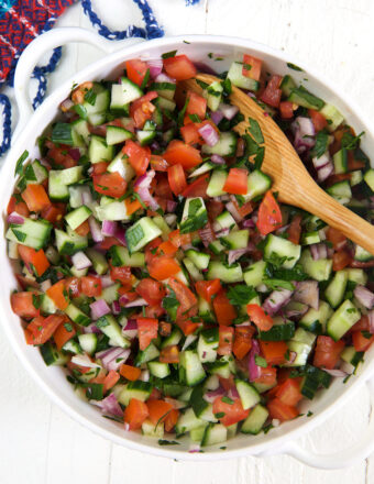 A large wooden spoon is placed in a bowl full of shirazi salad.