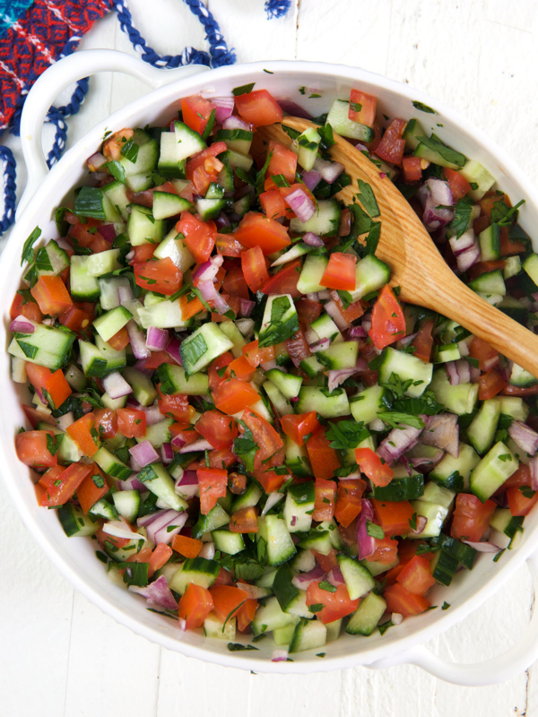 A large wooden spoon is placed in a bowl full of shirazi salad.