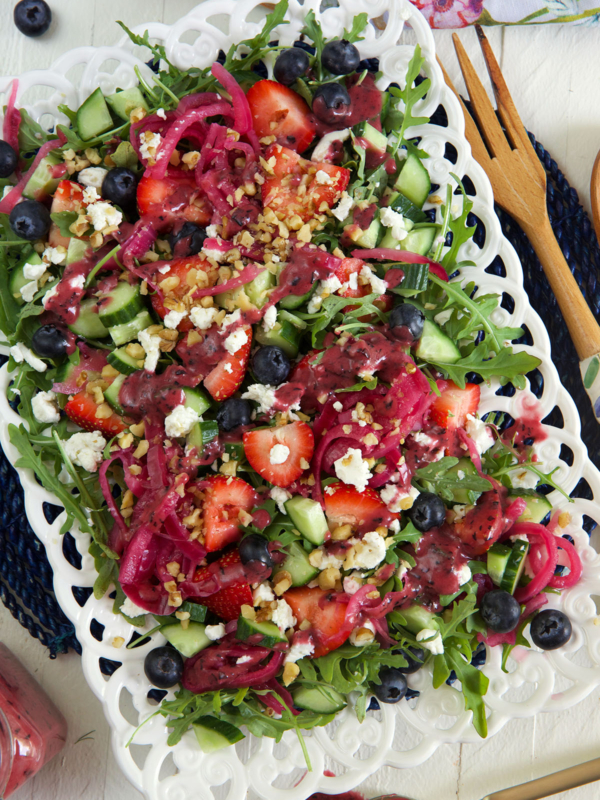A white serving plate is topped with strawberry arugula salad.