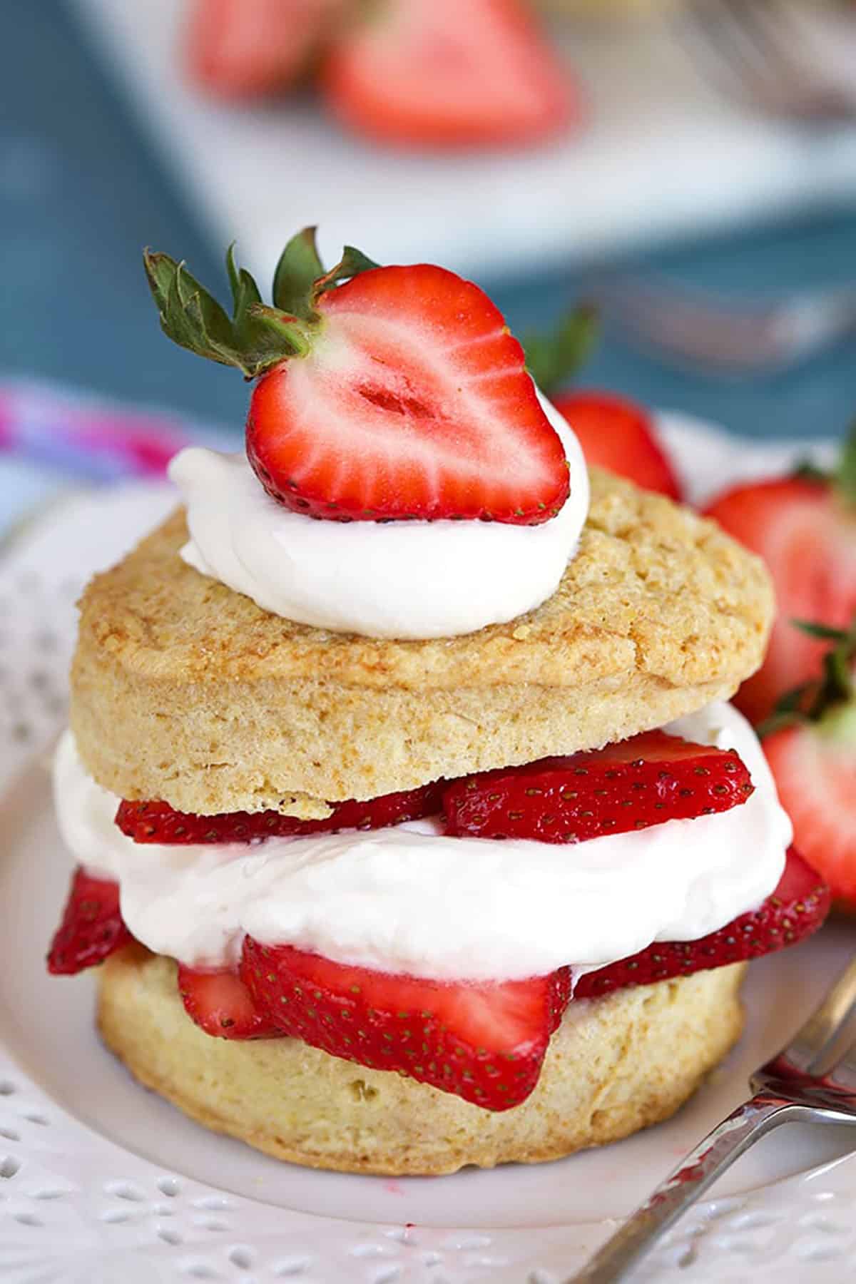 Close up of the very Best Strawberry Shortcake recipe on a white plate with a silver fork on a blue background 