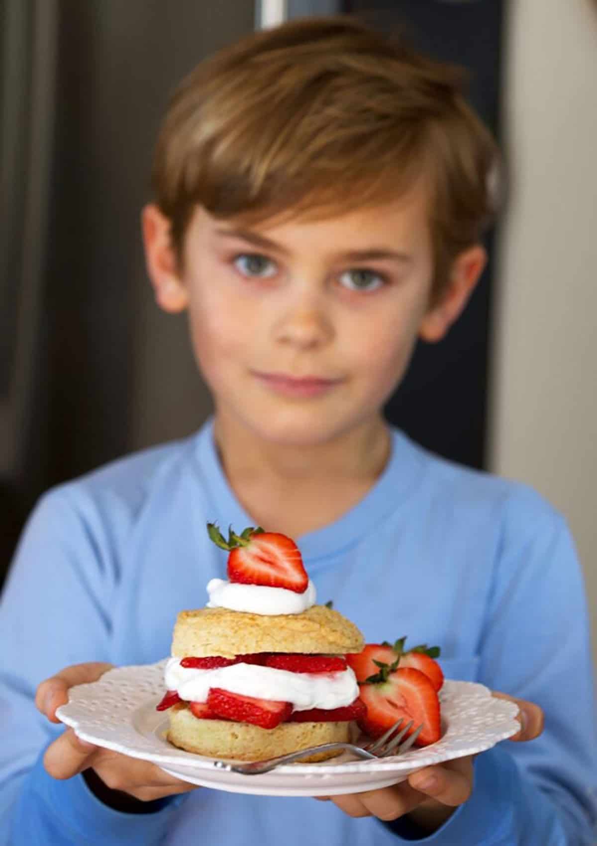 Landon holding on of the very Best Strawberry Shortcake recipe on a blue plate