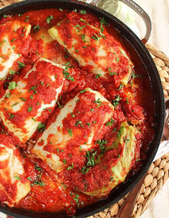 Overhead shot of stuffed cabbage rolls in a black le crest pan on a wicker placemat.