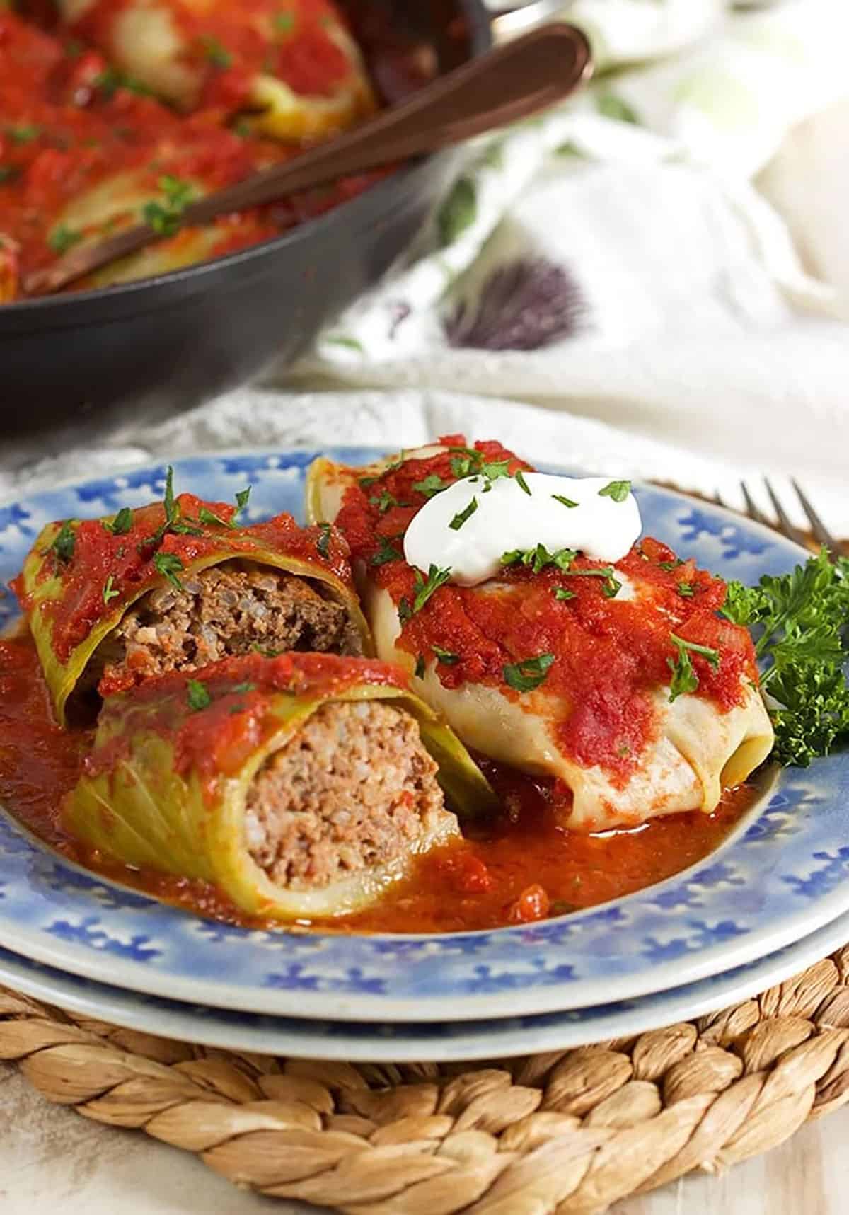 two stuffed cabbage rolls on a blue plate, one cut in half and the other has sour cream on top.