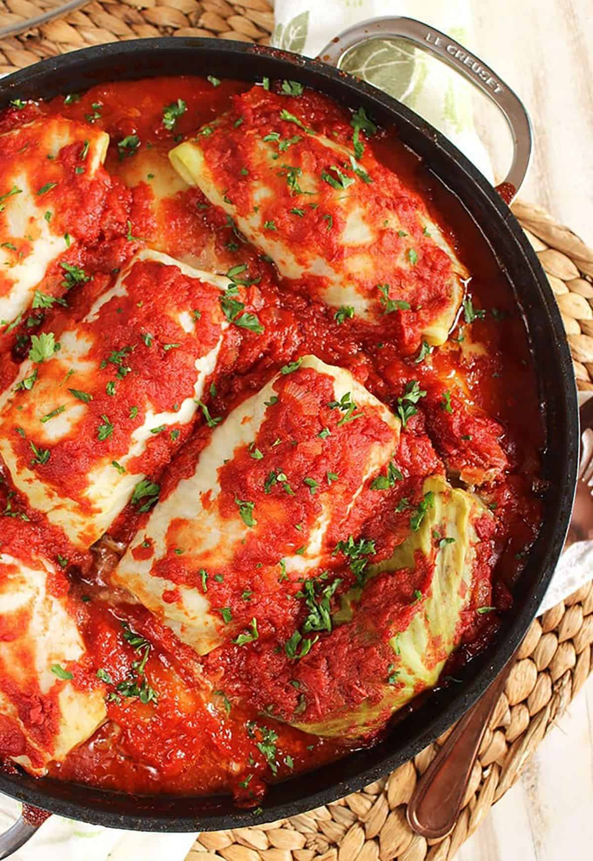 Overhead shot of stuffed cabbage rolls in a black le crest pan on a wicker placemat.