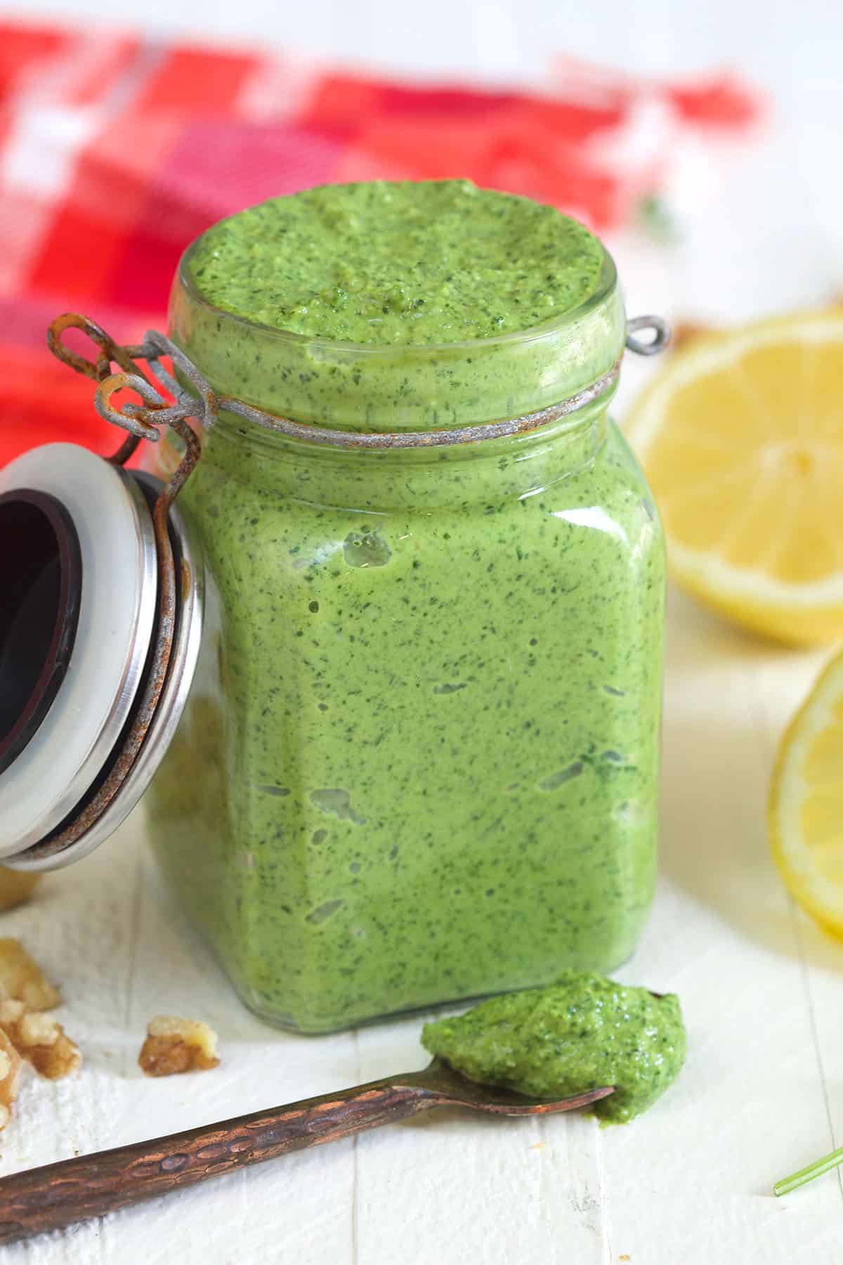 An open jar of pesto is placed next to a spoon with more pesto on it.