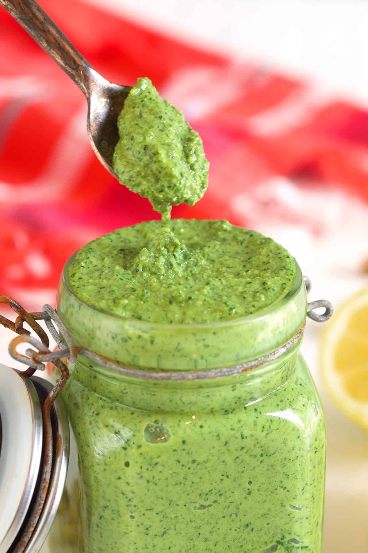 A spoon is lifting a small portion of pesto from the jar.