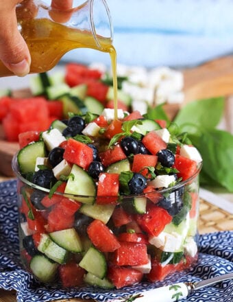 Watermelon Feta Salad in a glass bowl with dressing being poured over top.