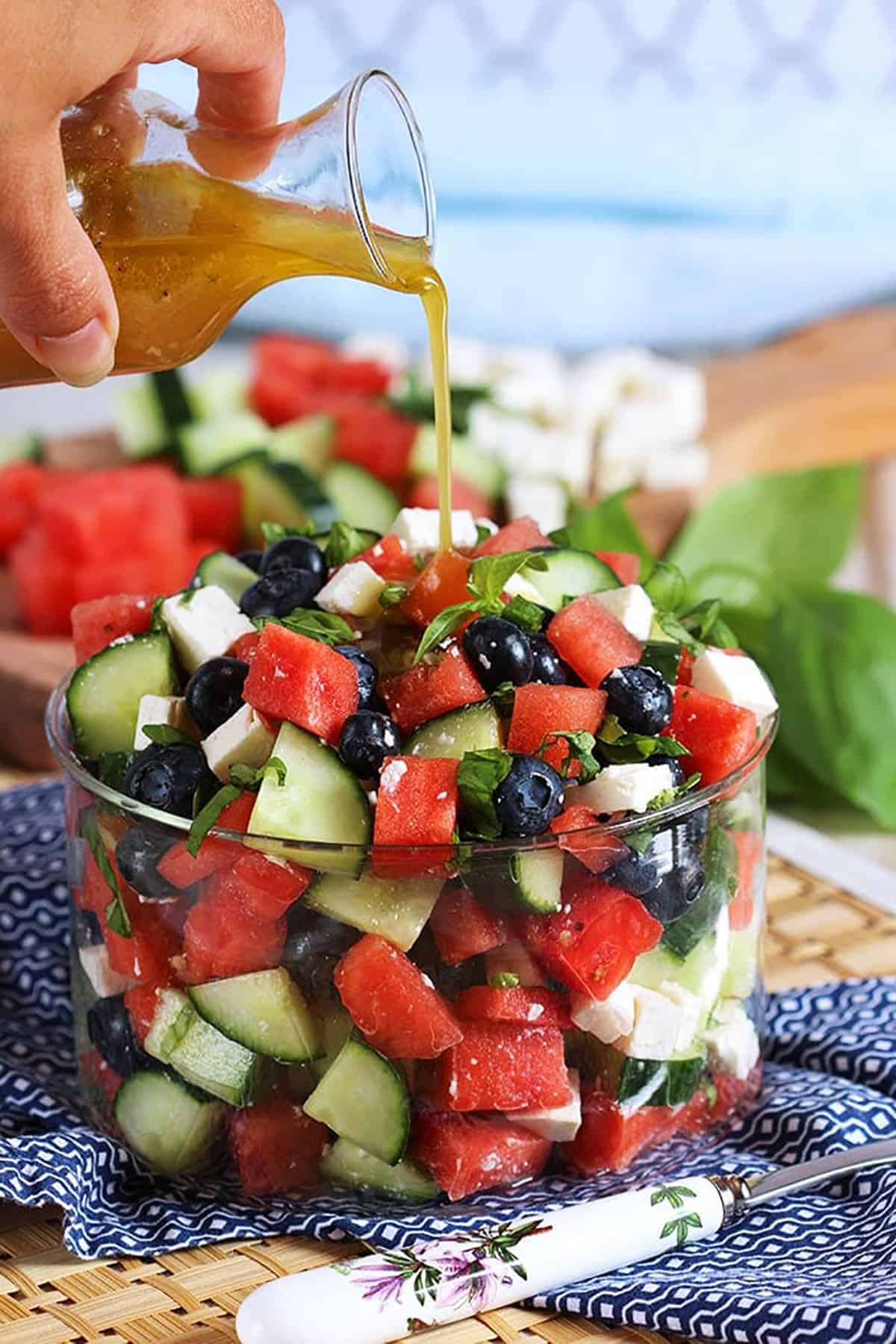 Watermelon Feta Salad in a glass bowl with dressing being poured over top.