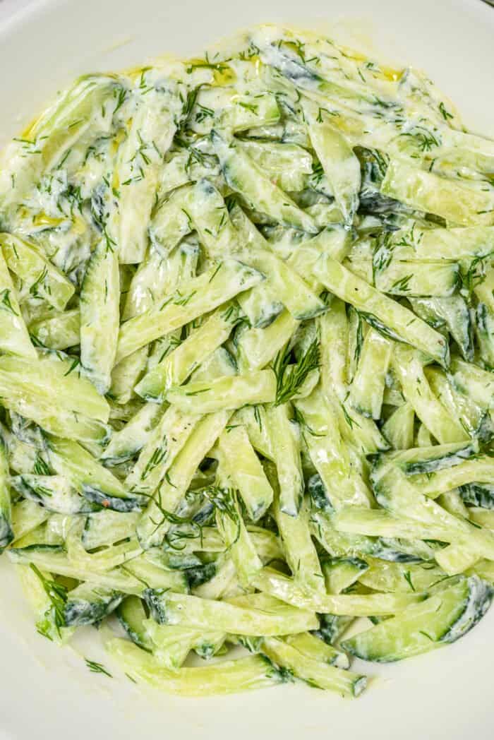 A freshly tossed cucumber dill salad is presented in a round white bowl.