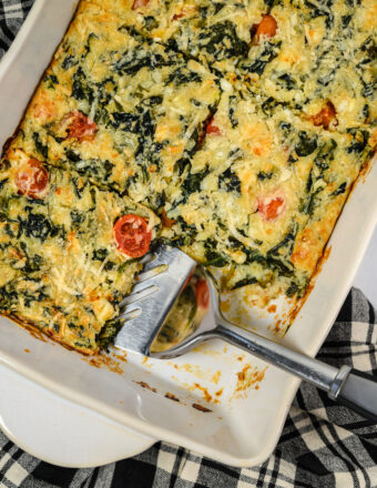 Spinach casserole is sliced and presented in a white baking dish with a spatula.