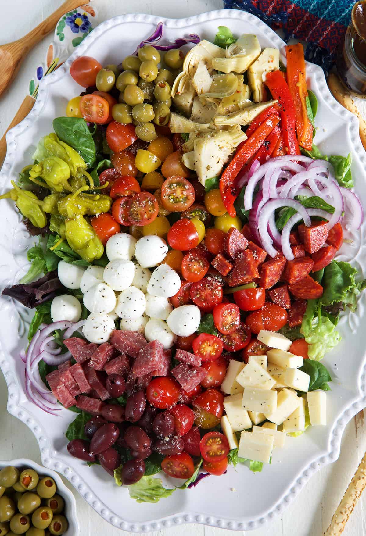 A white serving bowl is filled with antipasto salad.