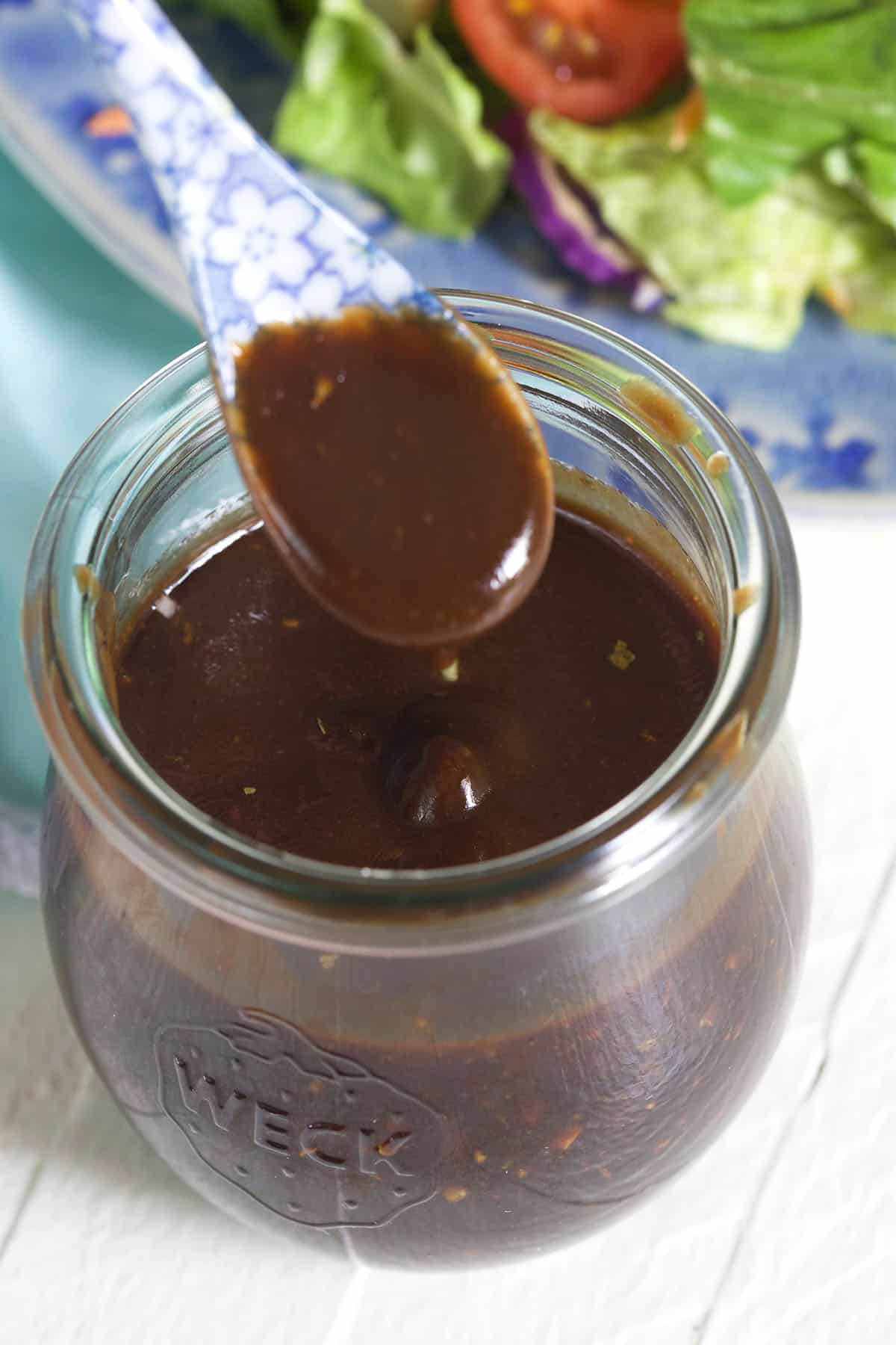 A spoon is held above a little jar of vinaigrette. 
