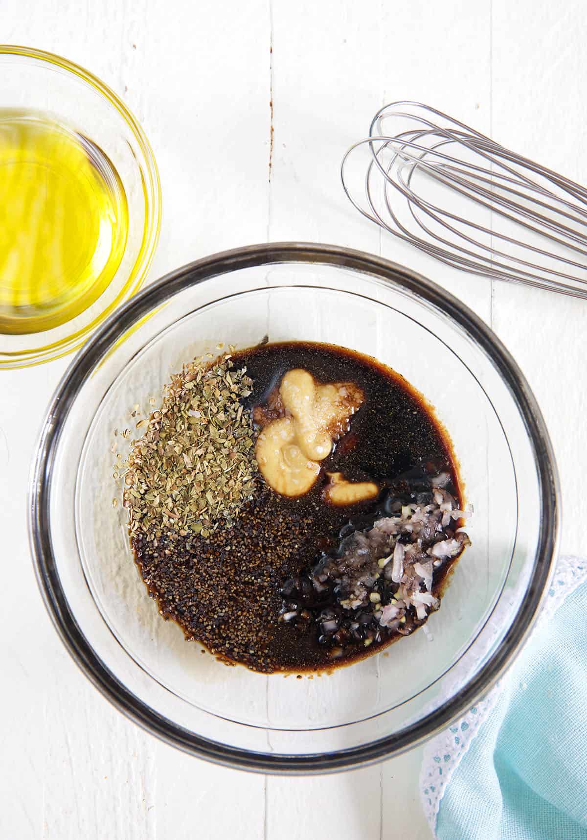 A glass bowl is filled with the ingredients for balsamic vinaigrette that have not yet been mixed.