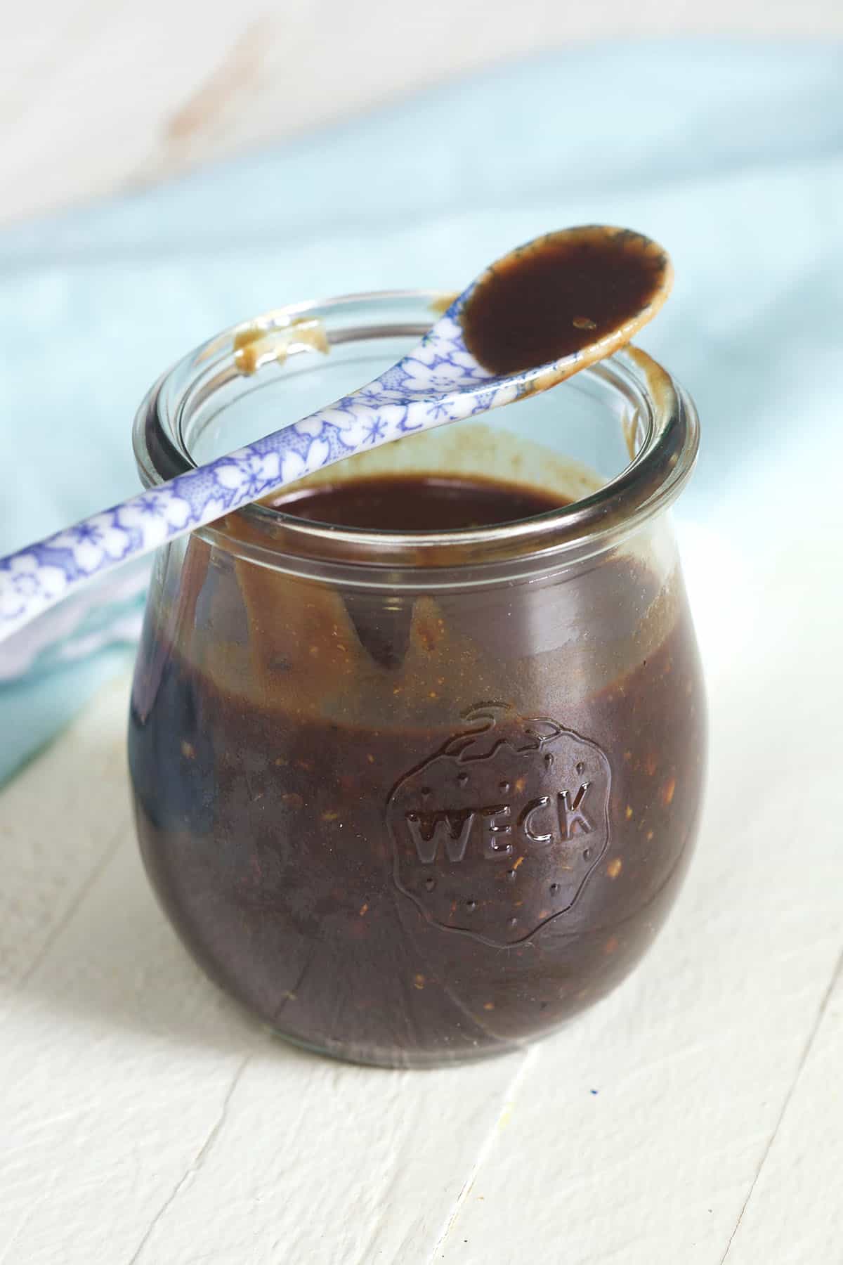 A small glass jar is filled with balsamic vinaigrette, and a small spoon is placed on top of the jar.