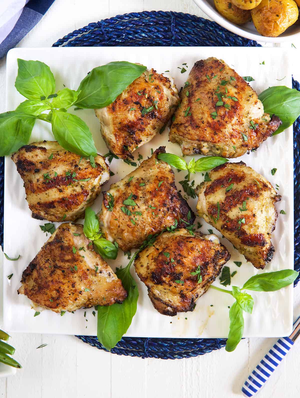 Several grilled chicken thighs are plated on a square white plate.