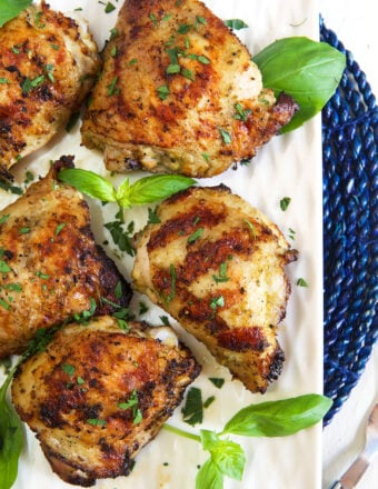 Several chicken thighs are garnished with fresh basil.