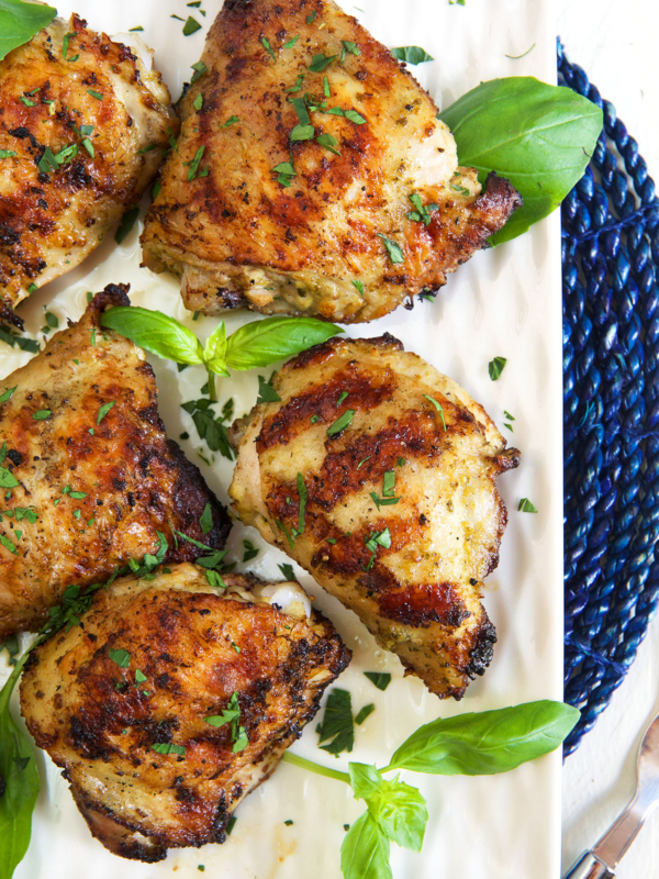 Several chicken thighs are garnished with fresh basil.