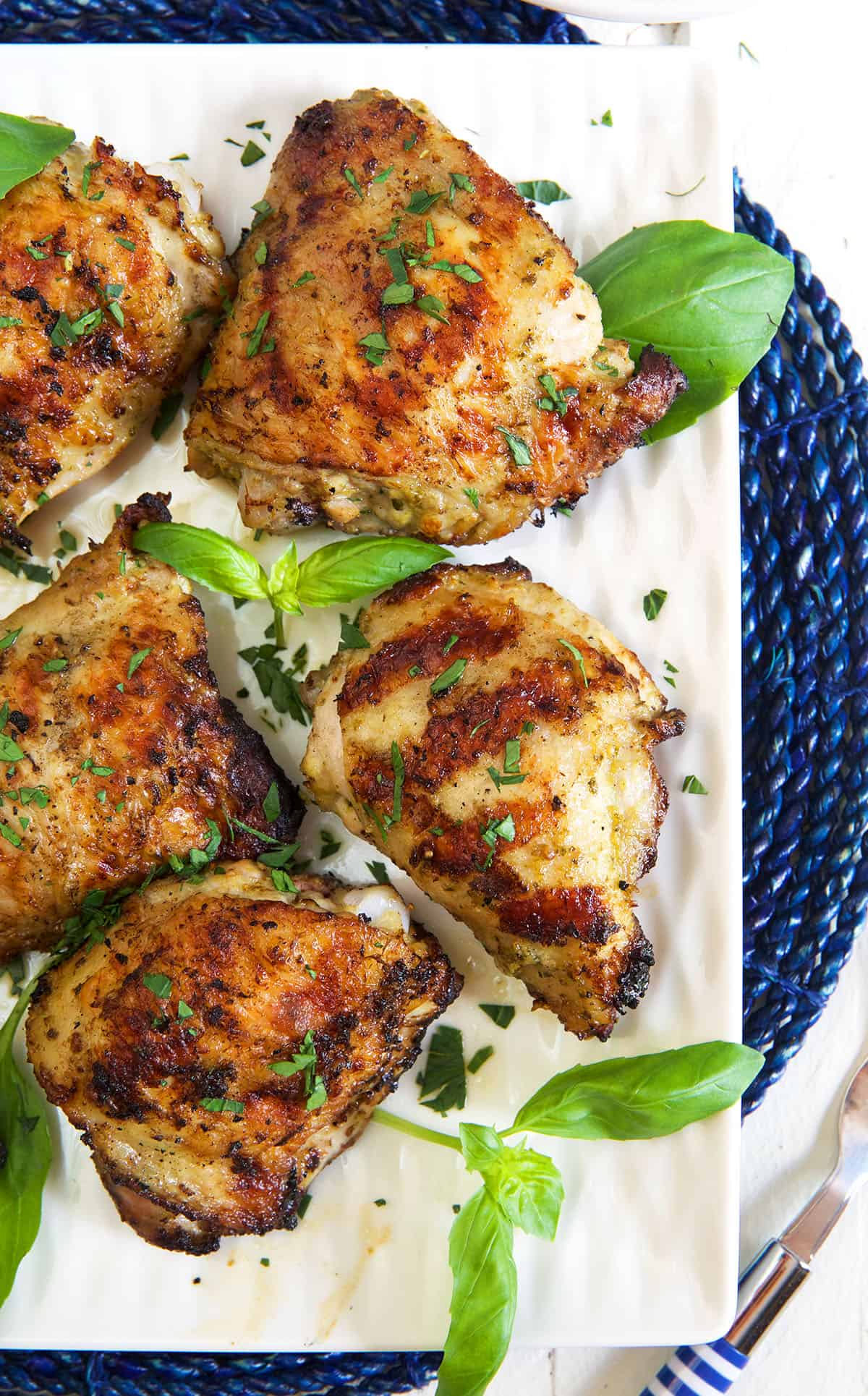 Several chicken thighs are garnished with fresh basil. 