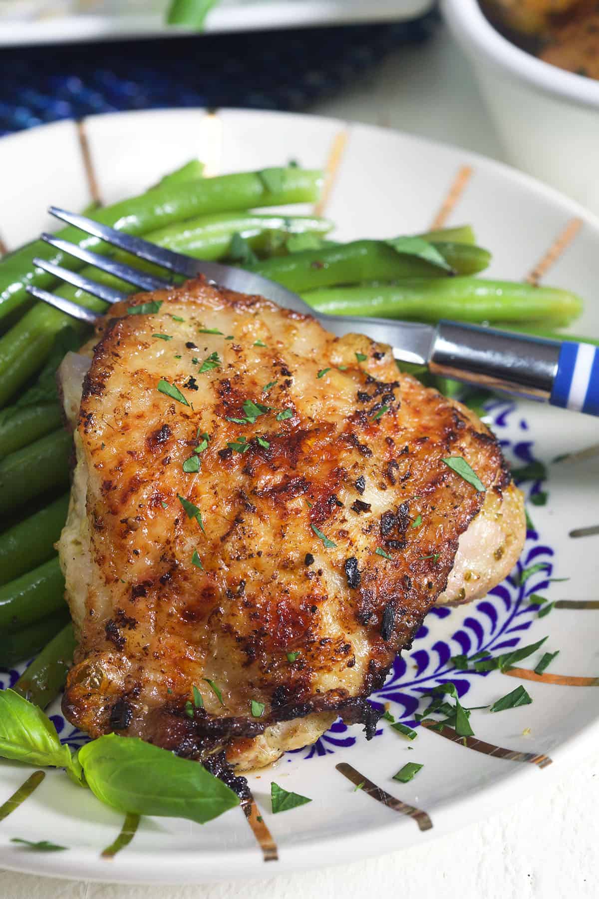 A blue and white plate is topped with veggies and a grilled chicken thigh.